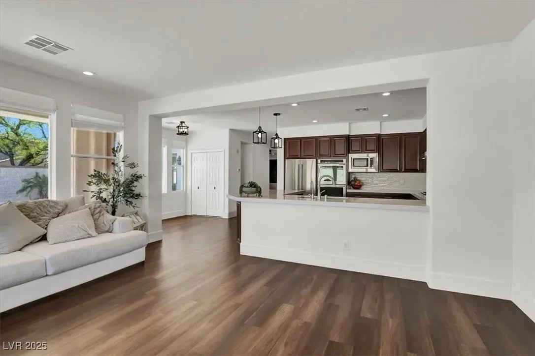 Bright open living room with a white sofa and wood floors, looking into a kitchen with dark cabinets.