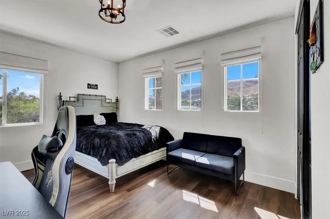 Bright bedroom with a white bed, black loveseat, three windows, and wood floors