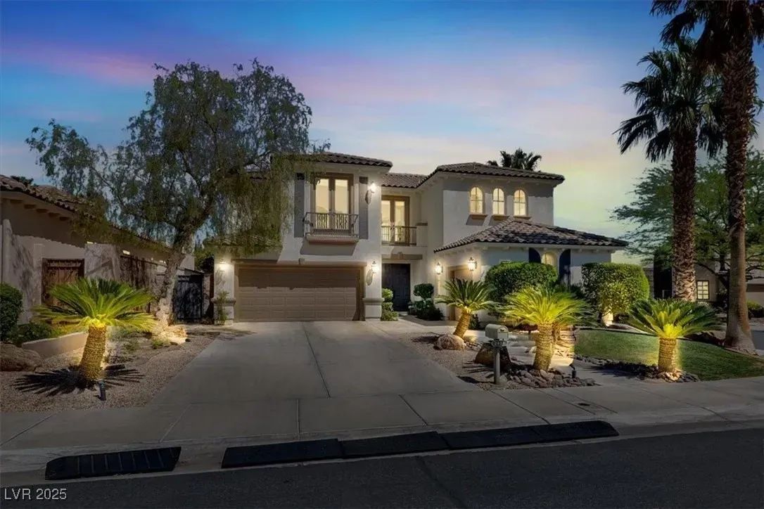 Modern two-story house at dusk with lit windows, palm trees, and a wide driveway