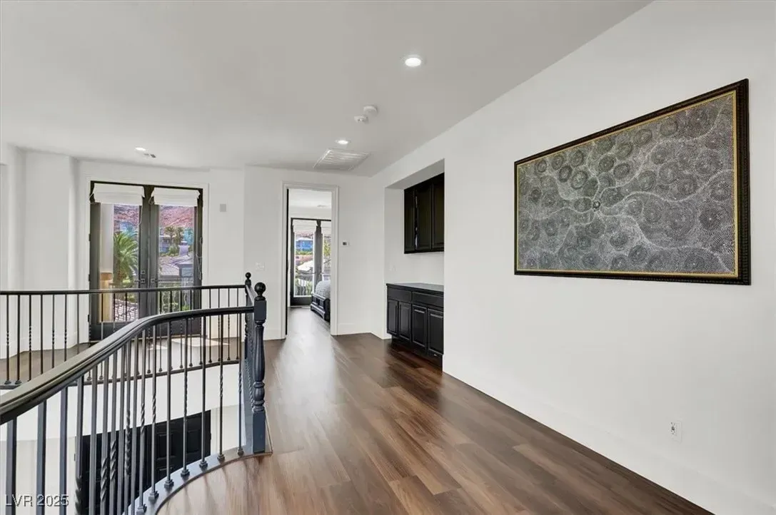Bright upstairs hallway with wood floors, white walls, black railing, TV, and framed wall art.