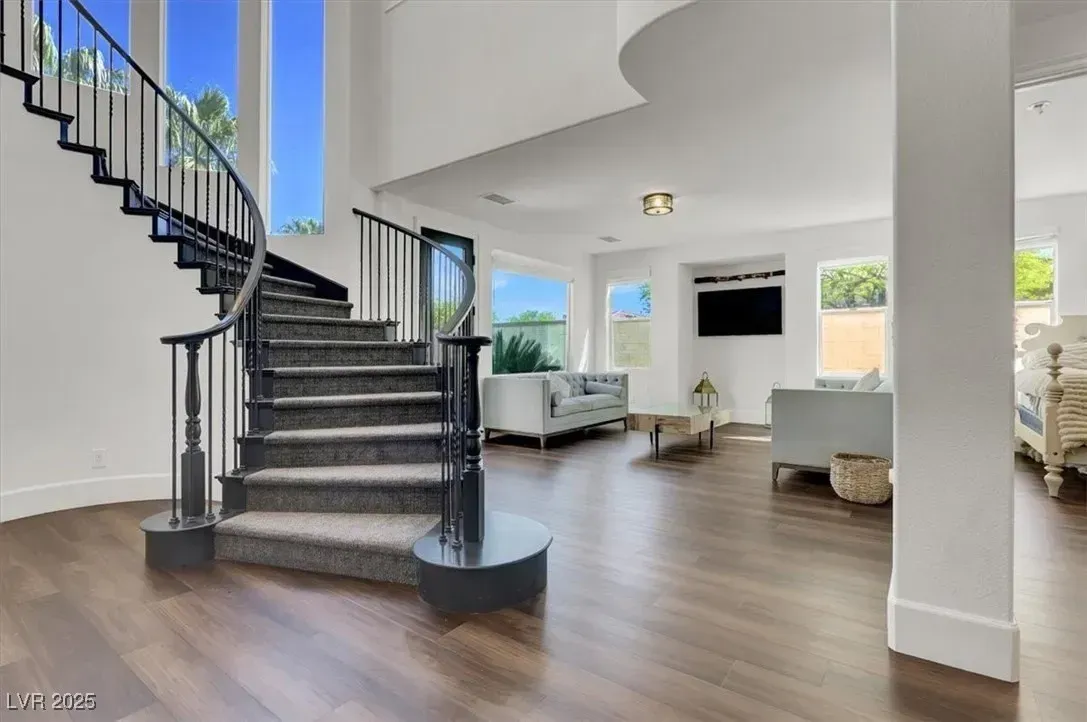 Modern open living room with curved staircase, wood floors, white walls, and large windows