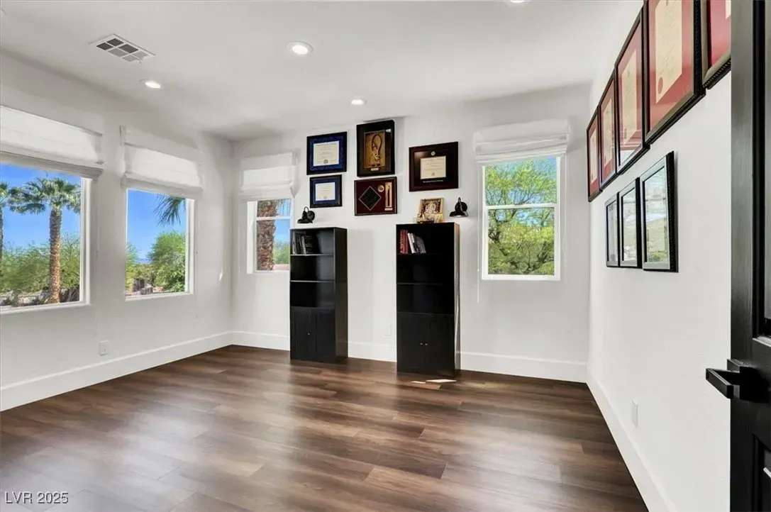 Bright empty room with wood floors, white walls, windows, and wall art displays