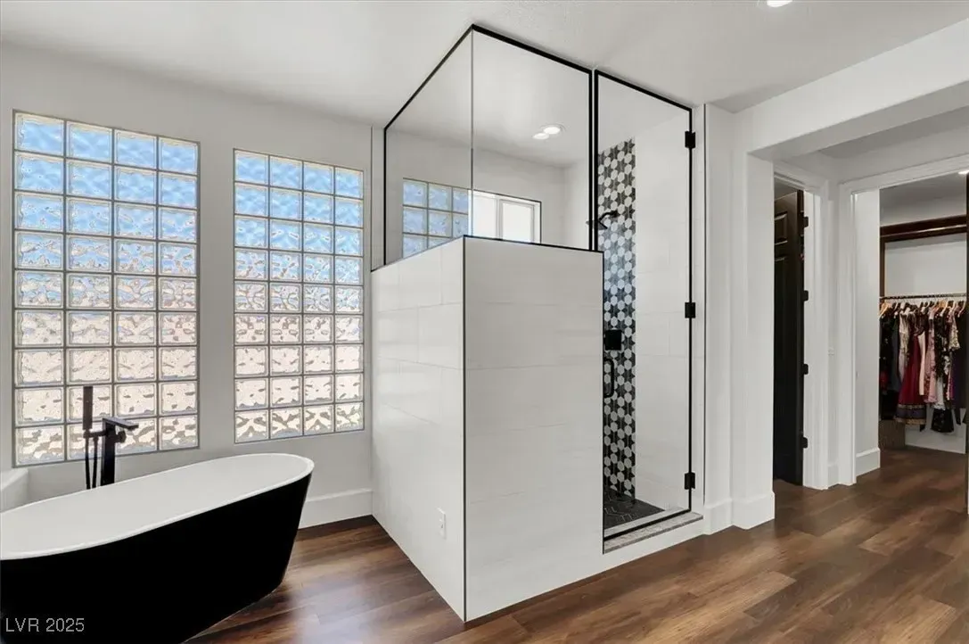 Modern bathroom with black-and-white tub, glass shower, frosted windows, and wood flooring