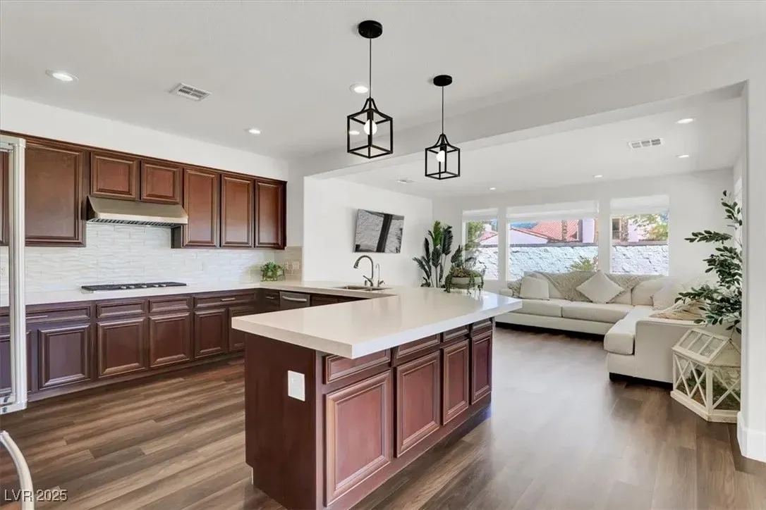 Bright open-concept kitchen and living room with dark wood cabinets, white island, and large windows