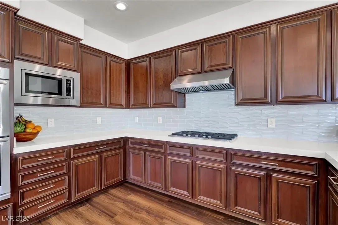 Modern kitchen with dark wood cabinets, stainless steel appliances, white tile backsplash, and wood flooring