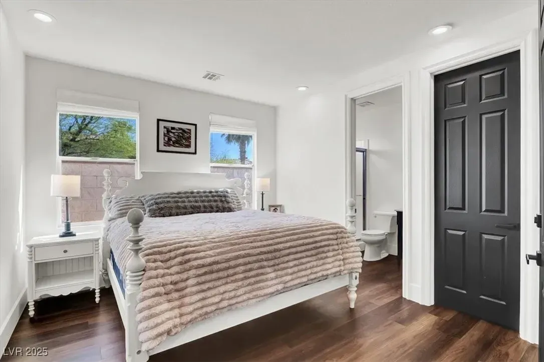 Bright bedroom with white bed, dark wood floor, white nightstands, and black closet doors.