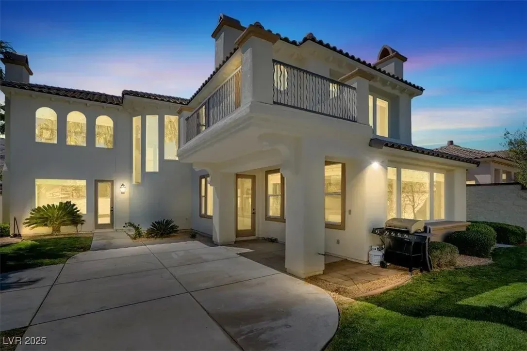 Modern two-story stucco house at dusk with lit windows, driveway, and manicured lawn