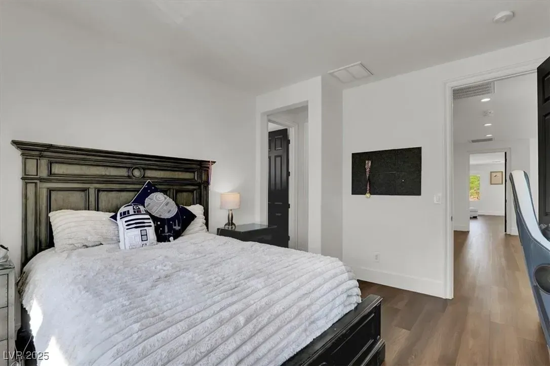 Bright bedroom with a large white bed, dark wood headboard, and open doorway to a hallway.