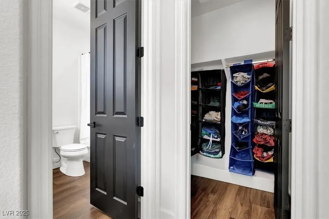 Open closet with organized hanging clothes beside a bathroom with a toilet and dark door