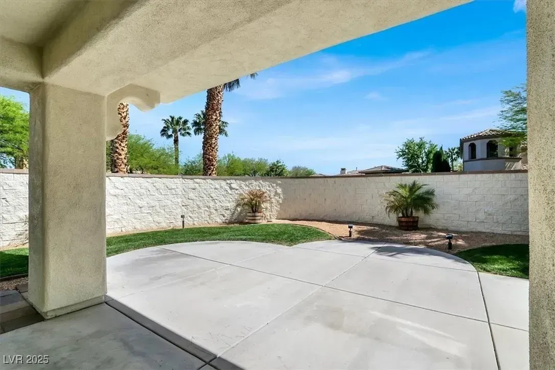 Covered patio overlooking a concrete courtyard, white wall, and palm trees under a bright blue sky