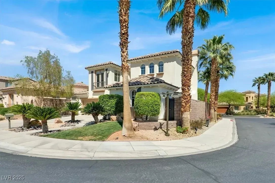Luxury house at a sunny street corner with palm trees, arched entryway, and desert landscaping
