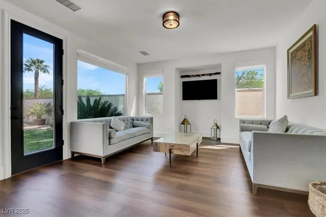 Bright modern living room with white sofas, wall-mounted TV, and large windows overlooking greenery