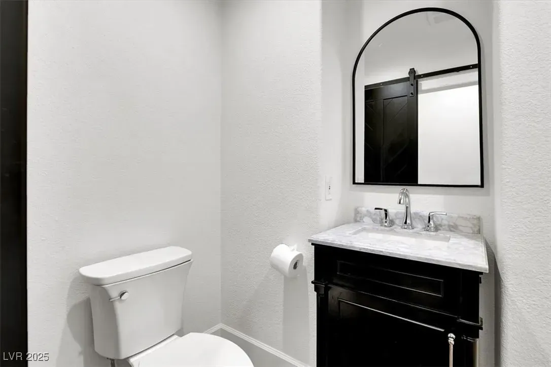 Small white bathroom with toilet, sink, black vanity, and arched mirror.