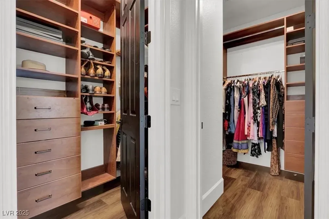 Walk-in closet with hanging clothes, drawers, and shelves in a bright white room.