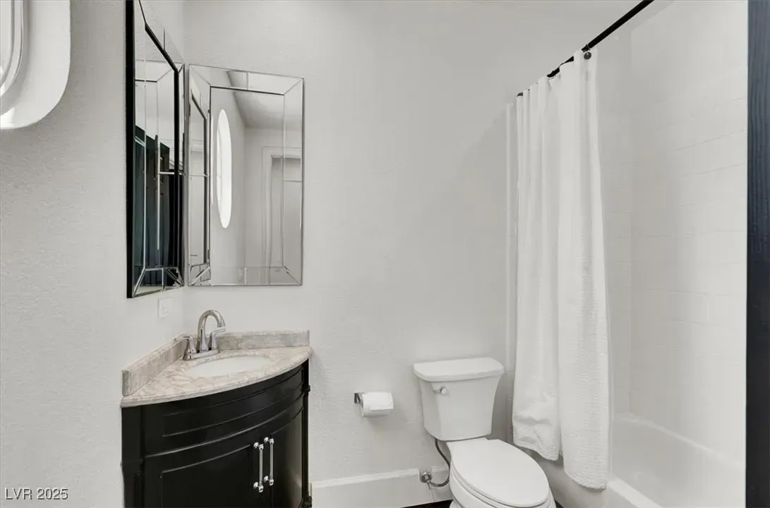 Small bathroom with a vanity sink, mirror, toilet, and bathtub with white shower curtain.