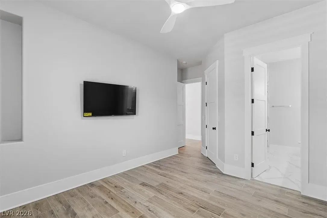 Empty white bedroom with wall-mounted TV, light wood floor, and open doorways