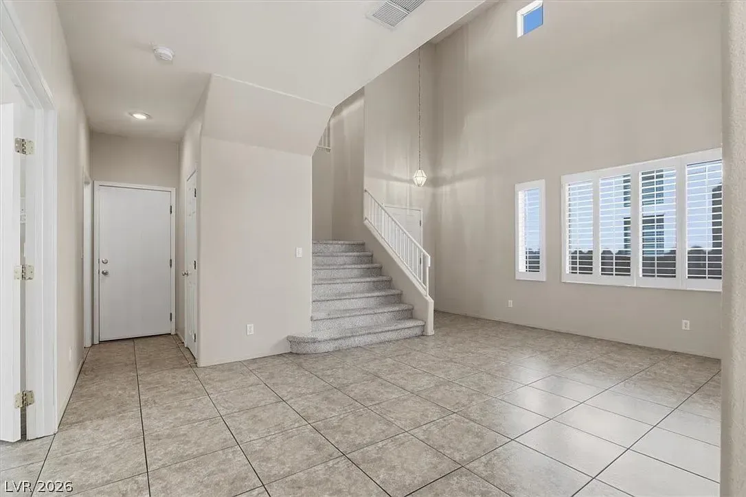 Bright empty foyer with tiled floor, staircase, high ceiling, and large windows
