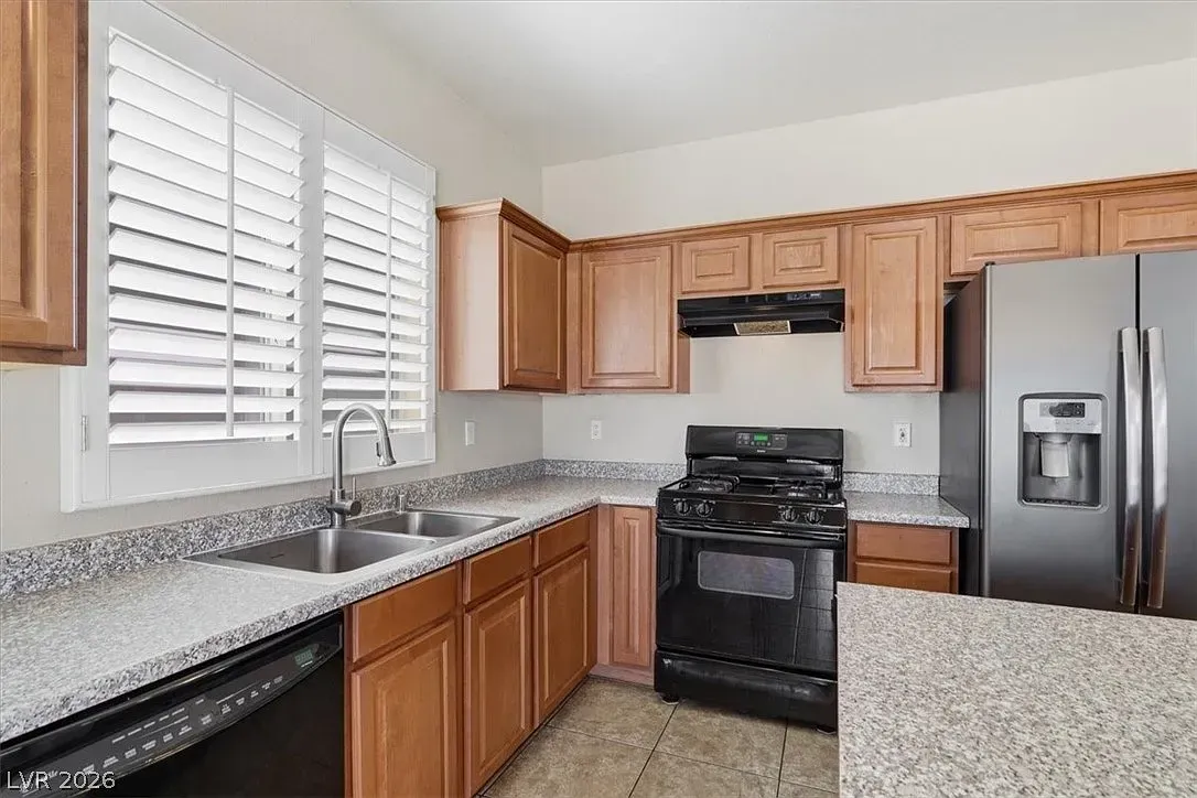 Modern kitchen with wood cabinets, granite countertops, stainless fridge, and black stove by a window