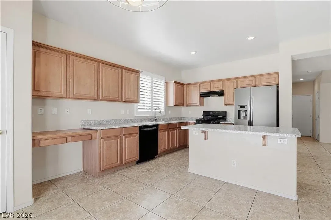 Bright kitchen with wood cabinets, white island, tiled floor, and stainless steel refrigerator