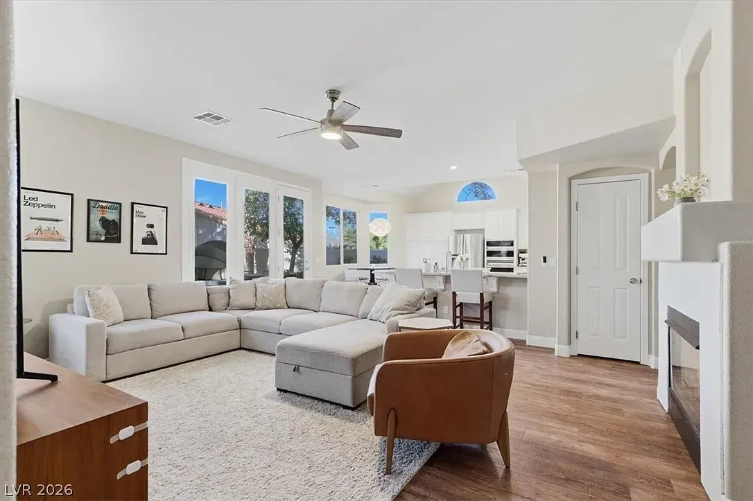 Bright, airy living room with sectional sofa, white chairs, wood floors, and large windows