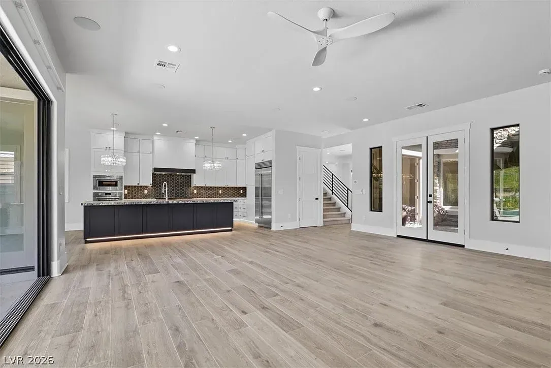 Modern open-concept living room with light wood floors, white walls, and a black kitchen island.