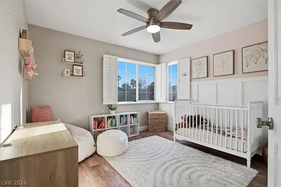Bright nursery with crib, white rug, window, and ceiling fan in soft gray tones