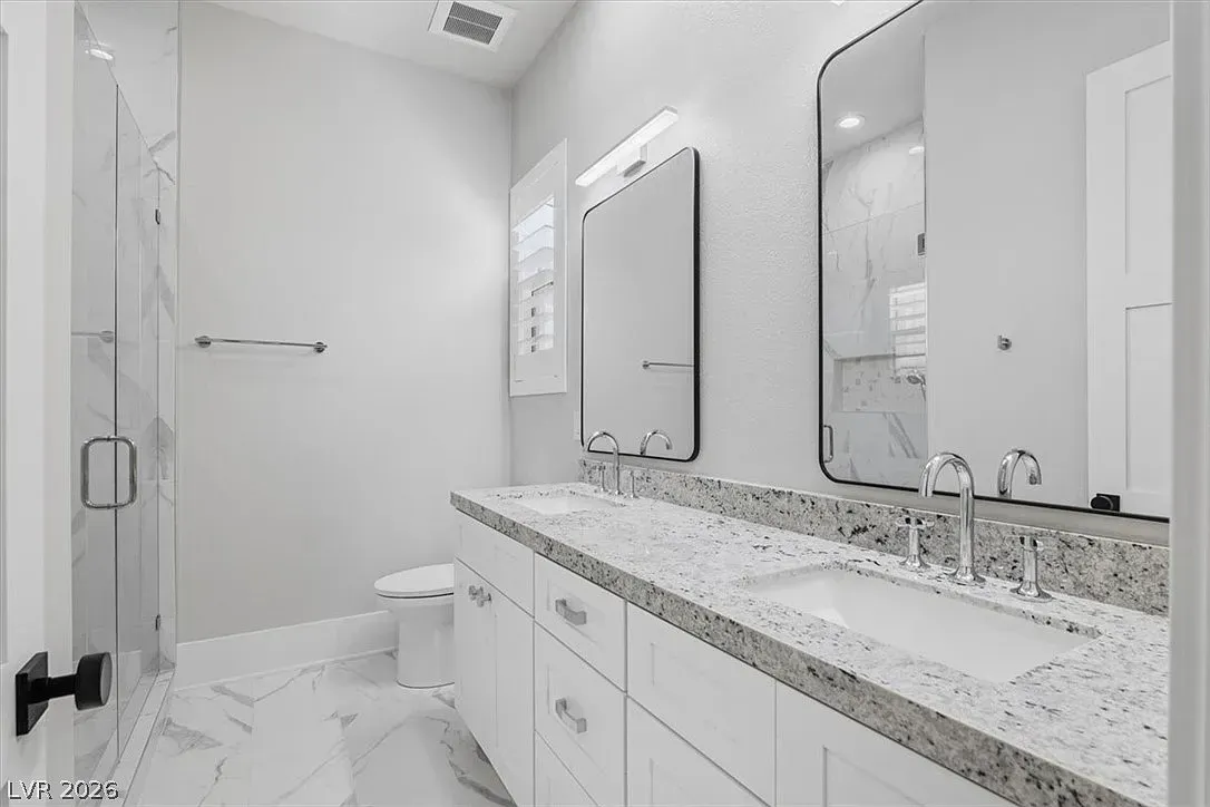 Bright modern bathroom with double vanity, large mirrors, white cabinets, and tiled shower.