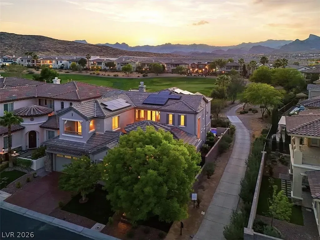 Dusk view of suburban homes and a winding path, with warm lights glowing and mountains in the distance