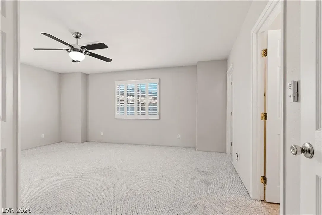 Empty light-gray bedroom with carpet, ceiling fan, window, and closet doors
