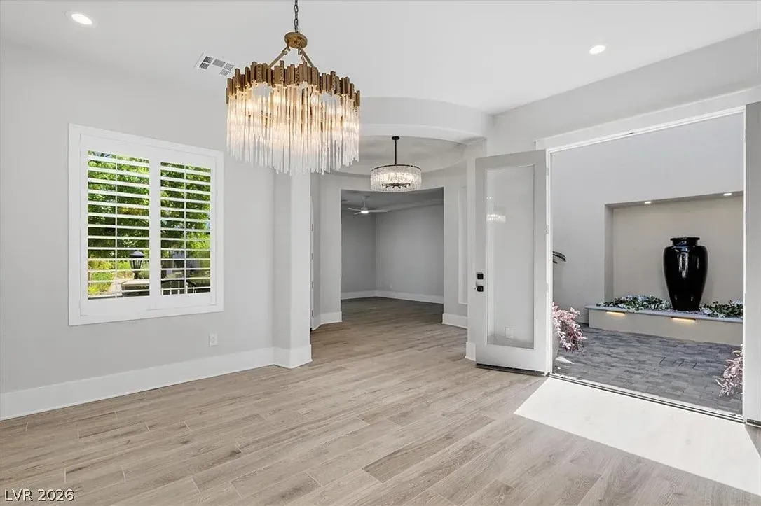 Empty bright room with light wood floors, white walls, chandeliers, and an open closet area.