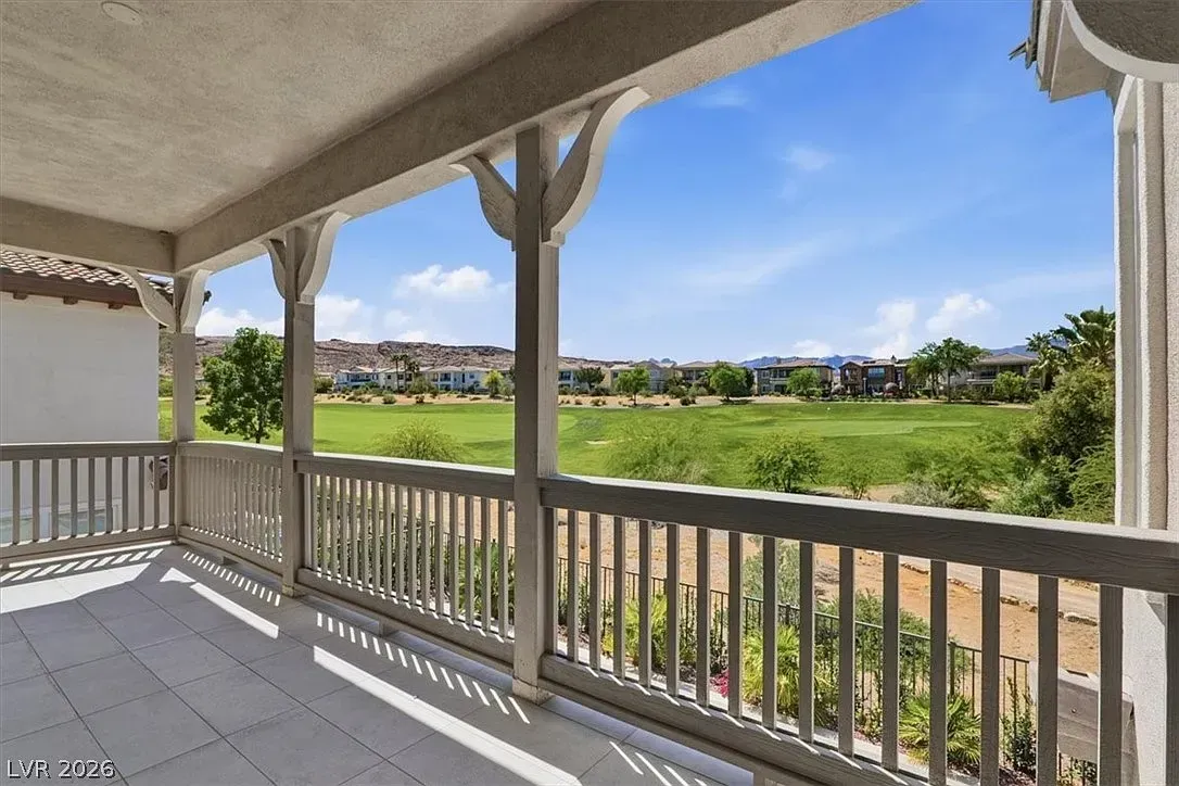 Covered porch overlooking a green field and distant homes under a blue sky