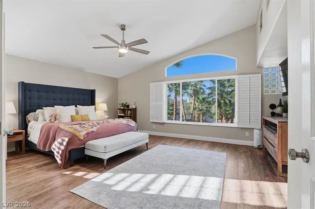 Bright bedroom with a navy headboard, pink bedding, large arched window, and sunlight on wood floors