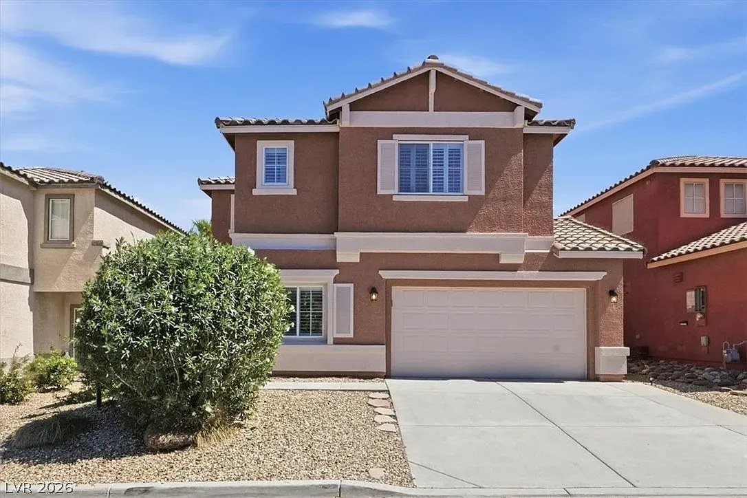 Two-story brick house with white garage and desert landscaping under a clear blue sky