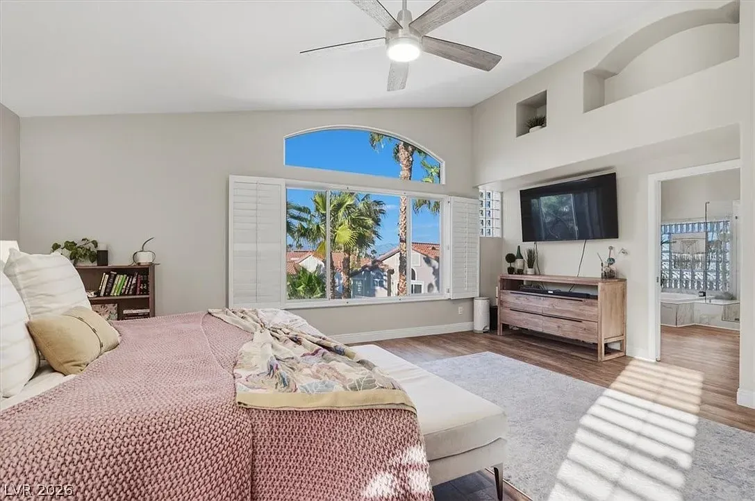 Bright bedroom with a large arched window, ceiling fan, TV, and a bed with pink bedding