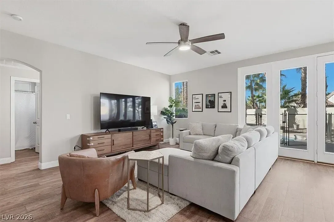 Bright living room with gray sectional, brown chair, TV console, ceiling fan, and French doors to a patio