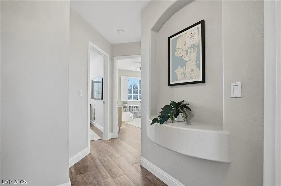 Bright hallway with gray walls, wood floors, arched niche, framed art, and a view into a sunlit room.