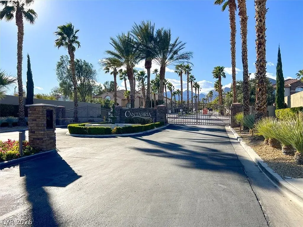 Palm-lined gated driveway leading to a residential entrance under bright sunlight