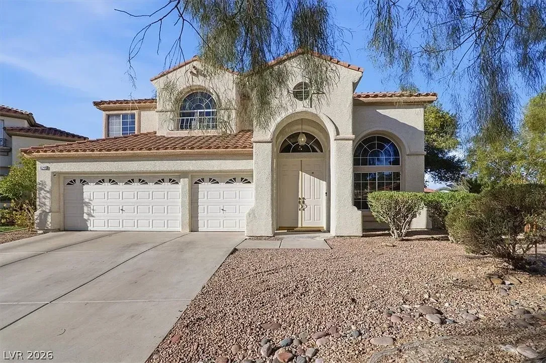 Two-story stucco house with a double garage, arched entry, and desert landscaping
