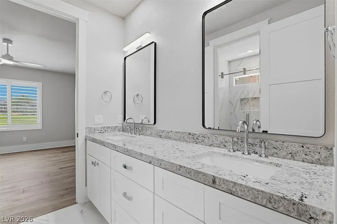 Modern bathroom vanity with white cabinets, speckled granite countertop, and large mirror next to a bedroom view.