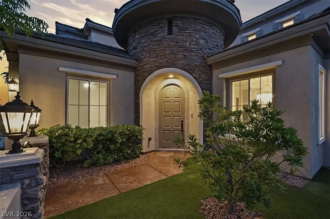 Front entrance of a stucco house at dusk, with lit doorway, stone facade, and landscaped walkway