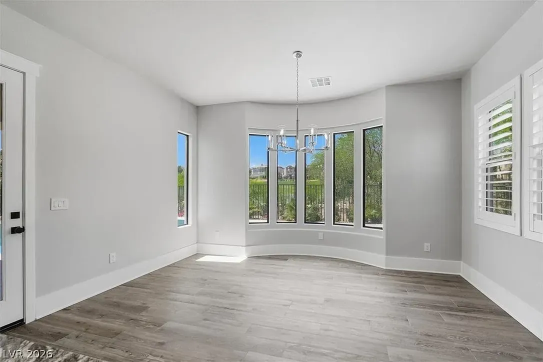 Empty bright living room with gray walls, large windows, and light wood flooring.