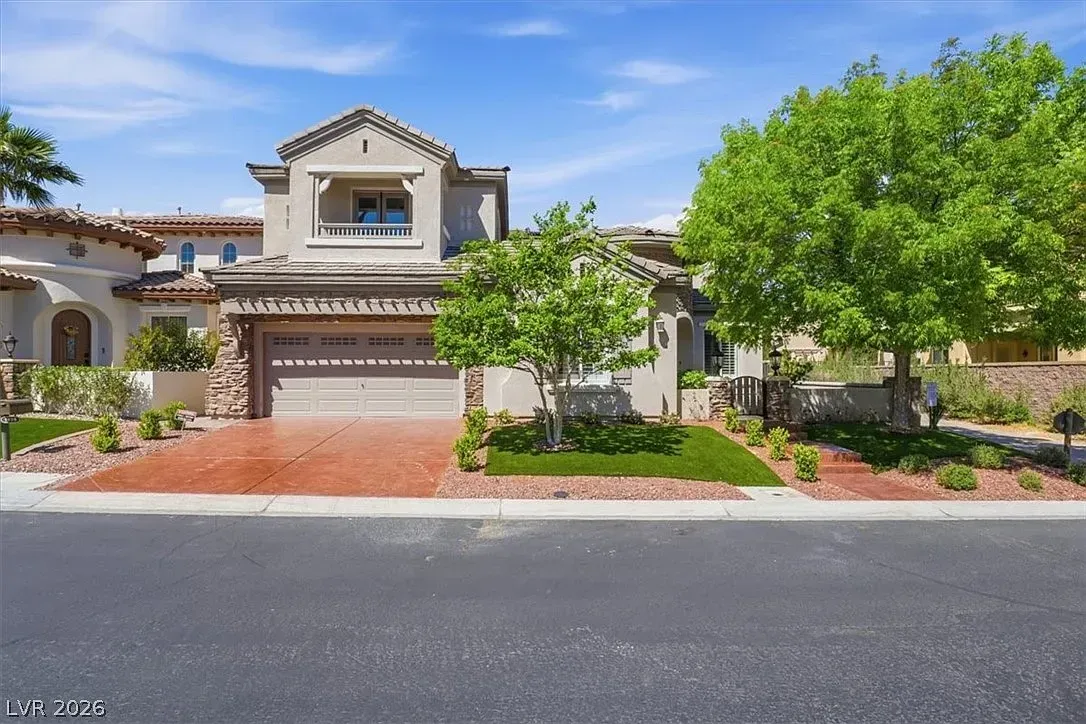 Mediterranean-style two-story house with a tiled roof, garage, and landscaped front yard under a blue sky