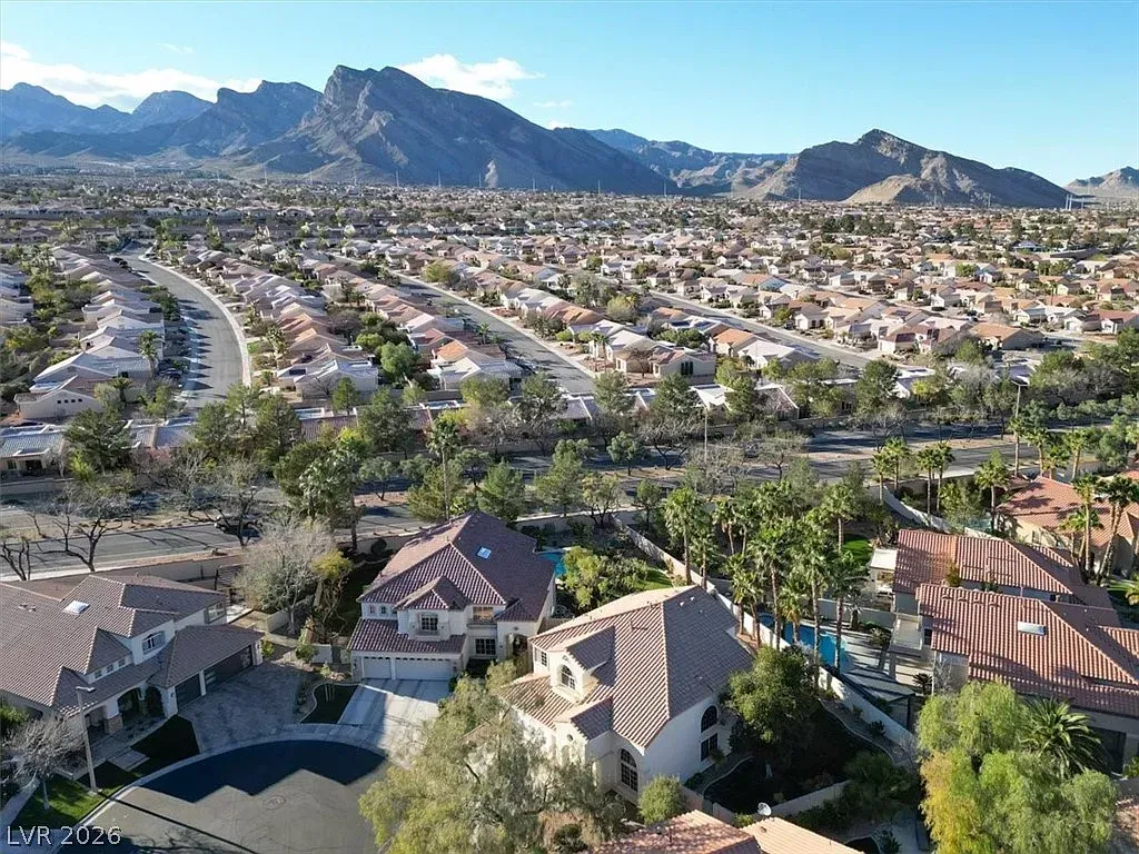 Suburban neighborhood with rooftops, palm trees, and mountains under a clear blue sky