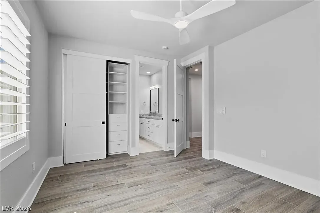 Bright empty bedroom with white walls, wood floors, closet, ceiling fan, and large window blinds