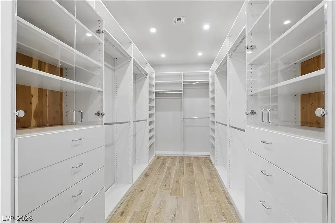 Bright white walk-in closet with shelves, drawers, and hanging space, centered on a wood floor aisle