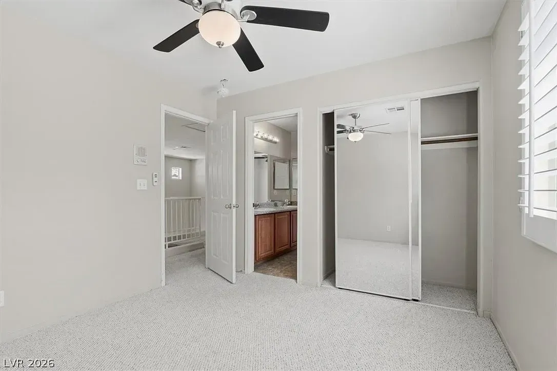 Empty white bedroom with ceiling fan, mirrored closet, and open bathroom doorway