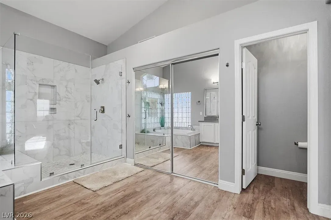 Modern bathroom with glass shower, sliding mirrored closet doors, and wood-look flooring