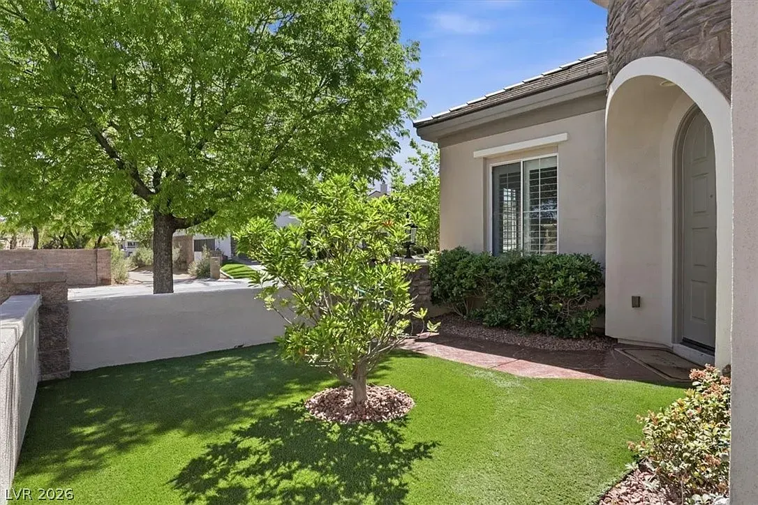 Front yard with green lawn, small tree, and stucco house entrance under bright sunlight