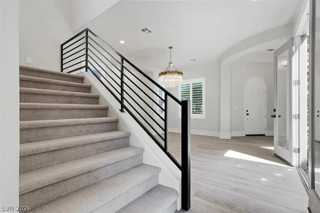 Bright entryway with carpeted stairs, black metal railing, and arched hallway windows