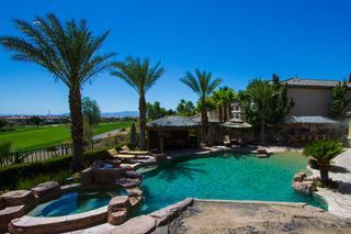 Luxury backyard pool with palm trees, stone waterfall, and desert landscape under a bright blue sky